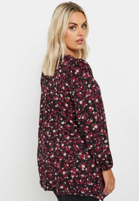 Svart blommig blus med långa ärmar; har röda och vita blommor, en lös passform och lätt volangdetalj vid axlarna.