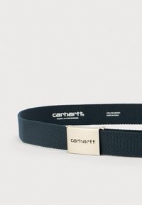 Cinturón de tela tejida de color azul oscuro con una hebilla metálica plateada que presenta el logo de Carhartt y texto de la marca dentro del lazo del cinturón.
