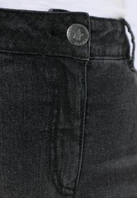 Vaqueros de mezclilla negra con textura suave, presentan un botón en forma de estrella plateada, trabillas para cinturón y un diseño clásico de bolsillo.