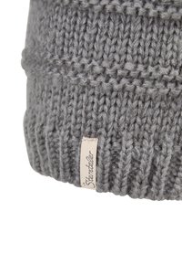 Close-up of the cuff of a thick, grey, knitted hat with a small fabric label sewn on the edge.