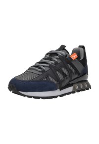 Zwarte en marineblauwe sport sneakers van mesh stof, met grijze veters, een witte zool en een oranje label met "CRU" aan de zijkant.