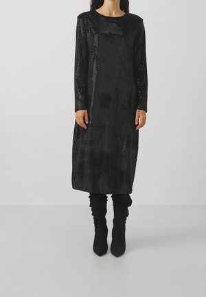 Langes schwarzes Kleid mit lockerem Schnitt, getupftem Muster, rundem Ausschnitt und langen Ärmeln, kombiniert mit schwarzen Stiefeln mit Absatz.