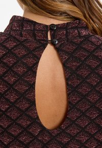 Black patterned top featuring a diamond design in dark red and metallic threads, with a keyhole opening at the back secured by two black buttons.
