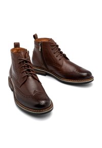Brązowe skórzane botki za kostkę z wzorem brogue, z sznurówkami i zamkiem bocznym. Gładka tekstura, zaokrąglony czubek i kontrastowa podeszwa.