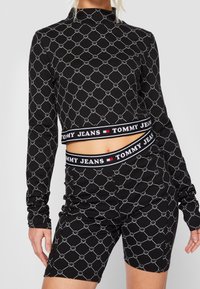 Svart långärmad topp och shorts-set med ett geometriskt smiley-ansikte mönster, med en märkesresår i kontrasterande färger. Slät tygtextur.