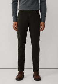 Pantalones de algodón verde oscuro con corte slim, que cuentan con bolsillos frontales, botones de metal y una textura suave. Combinados con zapatos de cuero marrón.