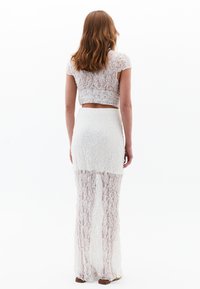 Ensemble deux pièces comprenant un crop top en dentelle blanche et une longue jupe en dentelle avec une partie supérieure doublée et une partie inférieure transparente.