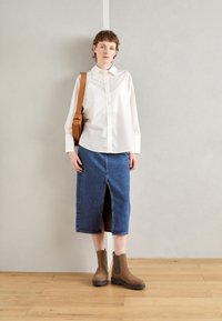 Hvit skjorte med lange ermer, mørk blå denimlepp med frontspalte, og brune ankelstøvler med robuste såler. Brun crossover-veske til stede.