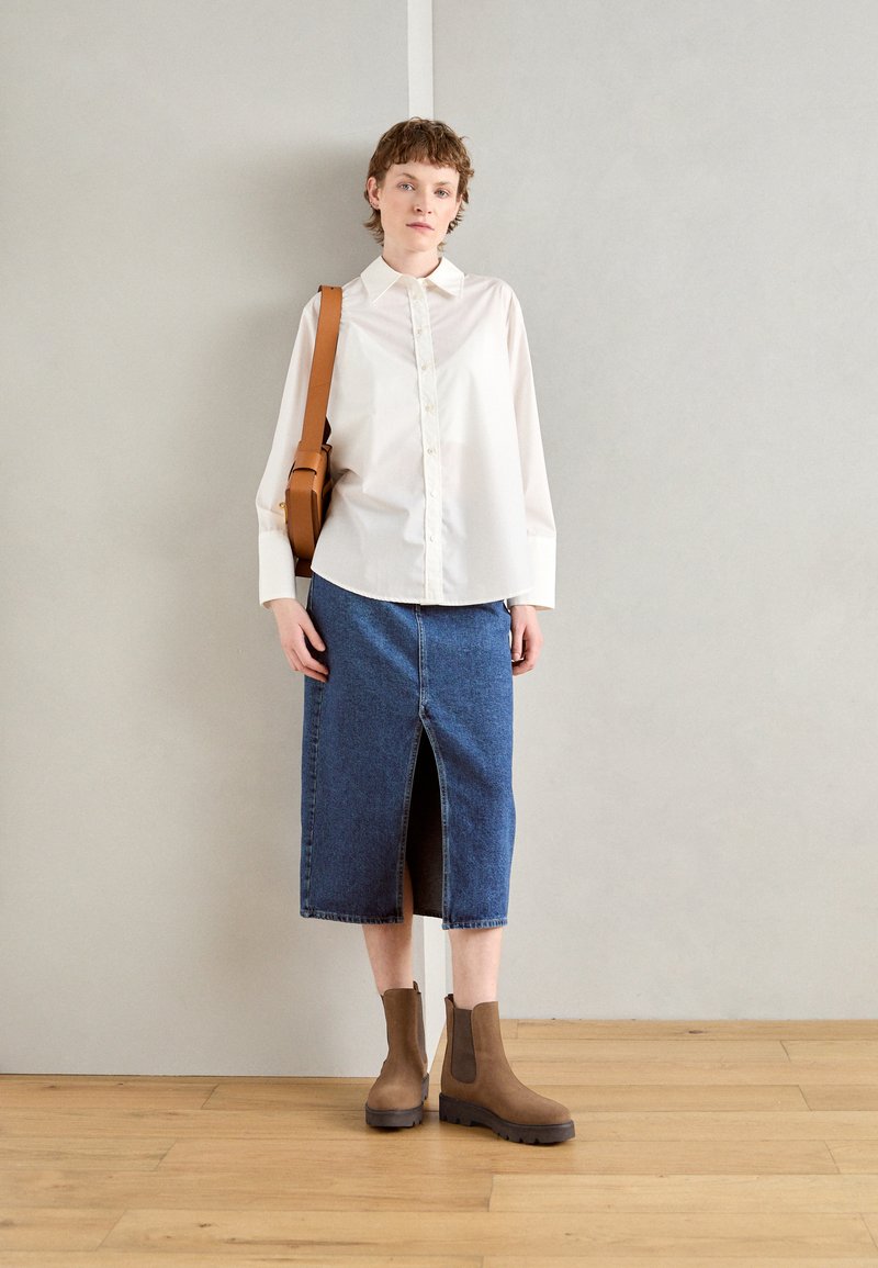 Weißes Hemd mit langen Ärmeln, dunkelblaue Jeansrock mit Schlitz vorne und braune Stiefeletten mit stabilen Sohlen. Braune Umhängetasche vorhanden.