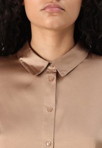 Bruine satijnen blouse met een klassieke kraag, voorzien van vijf knopen in een bijpassende kleur en een gladde textuur.
