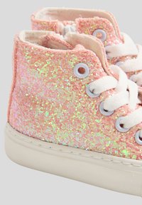 Różowe brokatowe trampki za kostkę mają błyszczące, fakturowane wykończenie, białe sznurowadła i okrągłe przelotki na gumowej podeszwie.