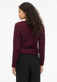 Mauve struktur sweater med et tredimensionelt mønster, lange ærmer og en tætsiddende talje. Parret med højtaljede sorte bukser.