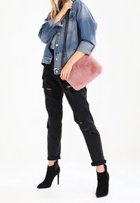 Růžová kabelka z umělé kožešiny obdélníkového tvaru, denimová bunda, černé roztrhané džíny a černé vysoké boty na podpatku nad kotníky, fotografováno na bílém pozadí.