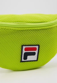 Pochette en tissu mesh vert vif avec une fermeture éclair sur le dessus et un écusson carré avec un logo rouge et noir sur fond blanc.