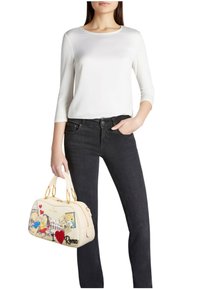 Borsa crema con disegni grafici colorati, due manici in tonalità oro e chiusura con cerniera. Modello che indossa una maglia bianca e jeans neri.