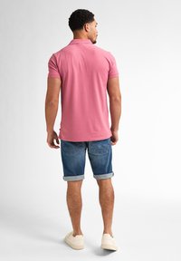 Chemise polo rose en coton, avec un col classique. Associée à un short en jean retroussé et des baskets de couleur claire.