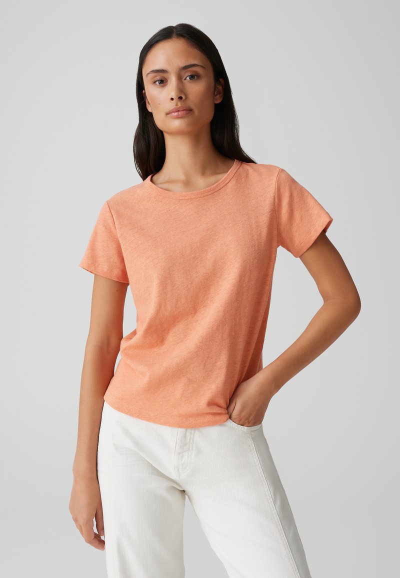 T-shirt arancione a maniche corte in tessuto morbido con scollo rotondo. Indossato con pantaloni bianchi, caratterizzati da una vestibilità comoda e una superficie liscia.