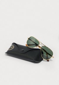 Occhiali da sole Ray-Ban con lenti verdi e montatura in metallo dorato, appoggiati su un astuccio in pelle nera con chiusura a scatto e logo impresso.