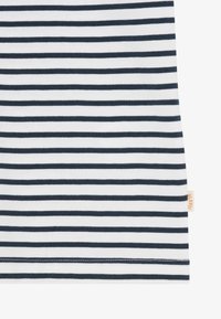 Tissu blanc avec des rayures horizontales noires uniformément espacées et une petite étiquette beige sur le côté droit près de l'ourlet.
