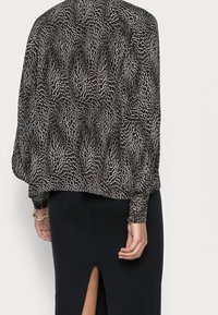 Mustavalkoinen kuvioitu paita, jossa on pitkät, pullistuvat hihat. Yhdistetty suunnikkaan muotoiseen hameeseen, jossa on sivuleikkaus. Rakeinen kangas.