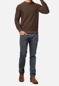 Brun strikket sweater med et tekstureret mønster, parret med grå slim-fit jeans og brune læder ankelstøvler. Enkel rund hals design.