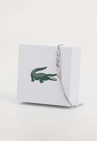 Silver bracelet with crocodile-shaped links on a textured white box featuring a green crocodile logo.