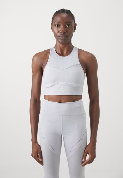 Világosszürke sportmelltartó, testhez simuló fazonnal és vékony pántokkal, ami passzol a perforált részletekkel ellátott, magas derekú leggingshez.