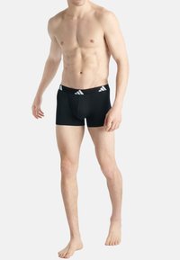 Svarta boxershorts med en bekväm midja som har en vit adidas-logotyp; figurnära design som betonar formen och en minimalistisk stil.