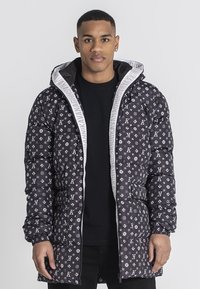 Chaqueta acolchada negra con un patrón repetido de logotipos blancos, con una capucha forrada de gris y cremallera, y puños elásticos para un ajuste ceñido.