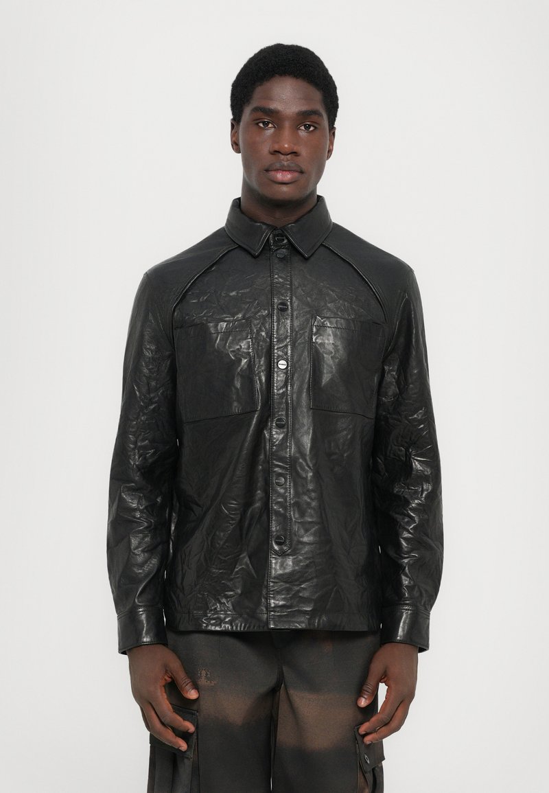 Black leather shirt with a glossy, crinkled texture; features a pointed collar, buttons, and two chest pockets.