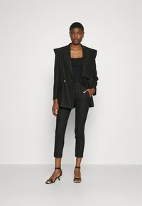 Melns svītrains uzvalks ar strukturētām plecēm, kombinēts ar melnu tanktopu un īsām pieguļošām biksēm, pabeigts ar melnām, siksniņām rotātām augstpapēžu kurpēm.