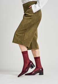 Culottes de ante color verde oliva con bolsillos laterales, combinados con calcetas transparentes burdeos y tacones de charol burdeos con punta afilada y tacón cuadrado.