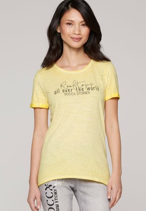 Yellow short-sleeve T-shirt with rolled cuffs, featuring black text "Rooftops all over the world SOCCX STORIES" on the front. Soft texture.