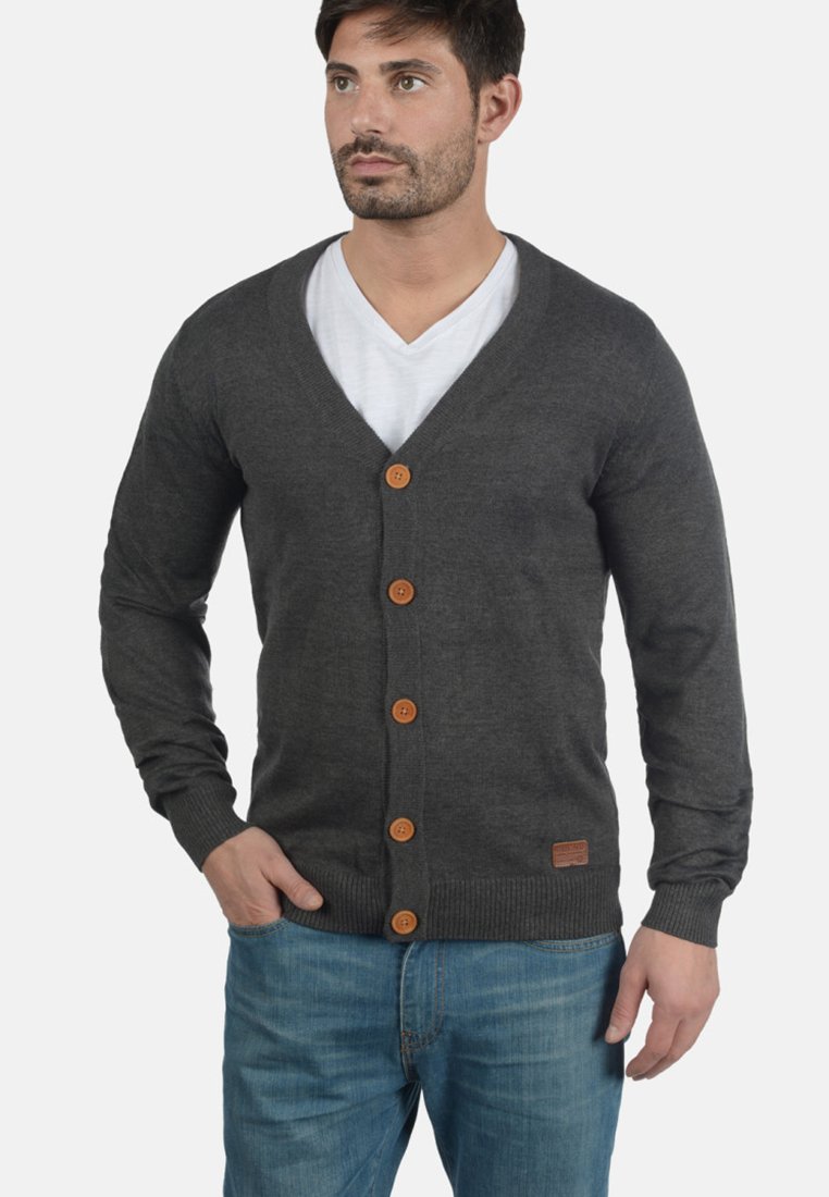 Kullgrå cardigan laget av mykt stoff med v-hals, lange ermer og treknapper, båret over en hvit v-hals skjorte.