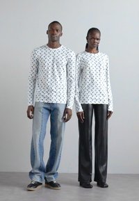 Vita långärmade skjortor med svarta halvmånemönster, kombinerat med ljusblå denim och blanka svarta byxor, båda bärda med avslappnade skor.
