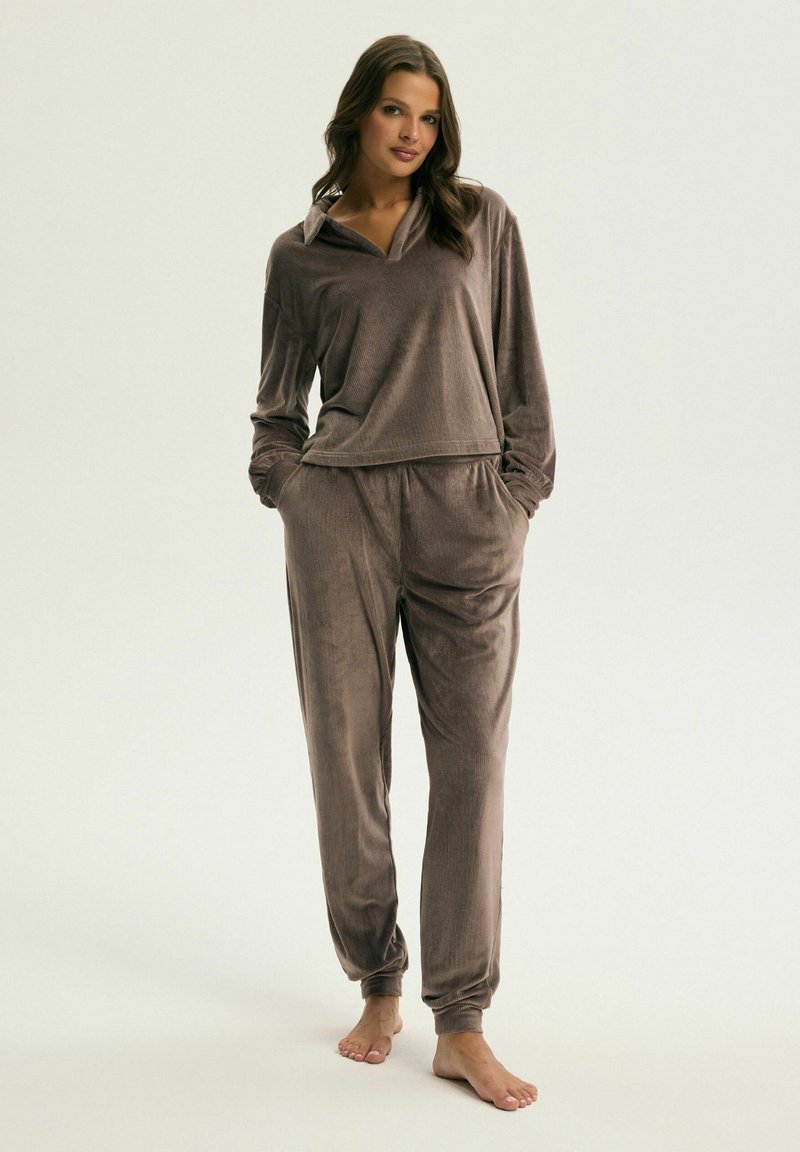 Brązowy zestaw dresowy z weluru, składający się z koszuli z kołnierzykiem i długim rękawem oraz spodni na elastycznej talii. Gładka tekstura, luźny krój, brak widocznych wzorów lub akcentów.