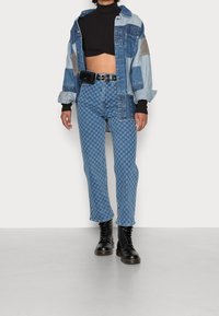 Oversized skjorta i denim med lapptäckesavsnitt; åtsittande svart polotröja; rutiga ljusblå jeans; svarta snörda kängor.