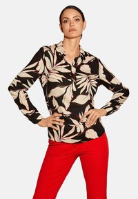 Long-sleeve black blouse with cream and red leaf patterns, featuring a collared neckline and button front, paired with red pants.