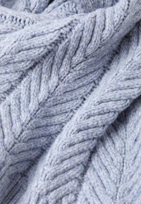 Tissu en tricot bleu clair avec un motif en chevron texturé, présentant un fil épais et volumineux. Apparence douce avec des fibres visibles et de la profondeur.