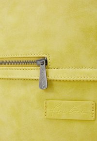 Żółta zamszowa torba z srebrnym zamkiem błyskawicznym i zawieszką z wytłoczonym logo marki. Gładka faktura z widocznym przeszyciem.