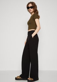 Oliven grønn crop top med korte ermer, kombinert med høyt liv sorte vide bukser og brune platåsandaler. Svart solbriller brukt.