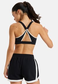 Sujetador deportivo negro con tirantes cruzados, con detalles en blanco; combinado con pantalones cortos negros con rayas blancas en los costados y un ajuste holgado.