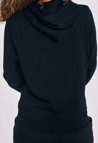 Svart hoodie med en avslappnad passform, featuring en rund huva och ribbad mudd. Slät textur, inga synliga logotyper eller mönster.