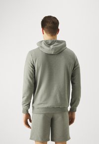 Felpa con cappuccio in grigio melange, caratterizzata da polsini e orlo a costine, con una vestibilità rilassata. Abbinata a pantaloni corti coordinati per un look completo.