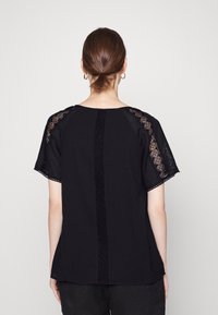 Blusa nera con maniche corte, dotata di dettagli in pizzo sulle spalle e un particolare in pizzo verticale sul retro. Tessuto morbido e testurizzato.