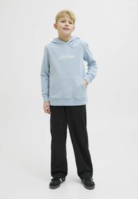 Felpa con cappuccio azzurra chiara, dotata di tasca frontale e testo del logo bianco, abbinata a pantaloni neri e sneaker nere. Design casual.