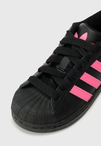 Svart lær sneakers med rosa detaljer, med fremtredende tre striper, teksturert tåhette og svarte snører.