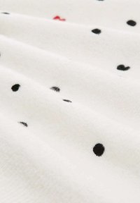 Materiał polarowy o białym tle, z rozrzuconymi czarnymi i jednym czerwonym kropkiem, prezentujący miękką, teksturowaną powierzchnię.