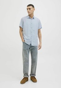 Camisa de botones de manga corta en azul claro, ajuste relajado, combinada con jeans grises claros y zapatos de ante marrón. Diseño simple, con mínimo hardware.