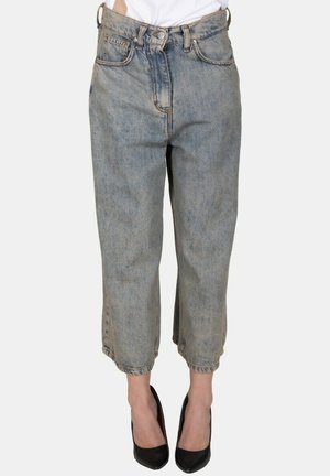 Persona che indossa jeans blu a vita alta, taglio largo e cropped con bottone e zip frontale, abbinati a décolleté nere chiuse.